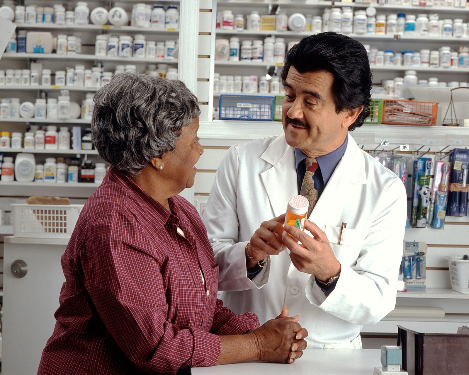 A woman talking with a pharmacist who is showing her a medicine bottle in a pharmacy.